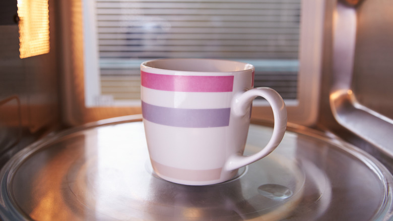 Reheating coffee in the microwave inside a pink, purple, and white coffee mug