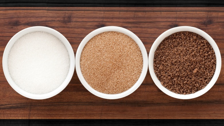 A bowl of white sugar, a bowl of light brown sugar, and a bowl of dark brown sugar.