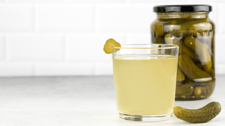 Pickle brine in glass in front of a glass jar of pickles.