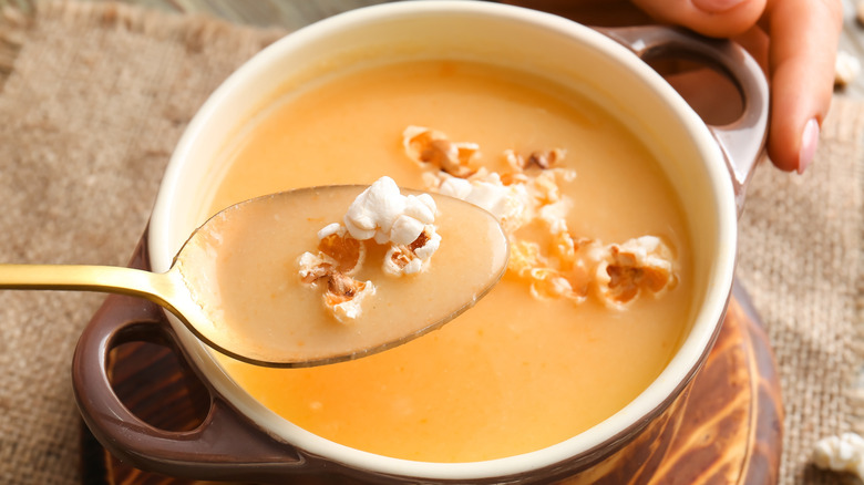 A bowl of yellow soup with popcorn on top and a spoon