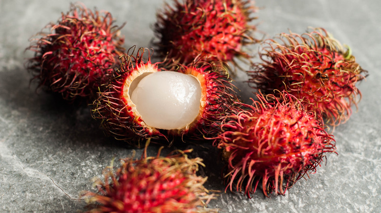 five whole and one opened rambutans on a stone countertop