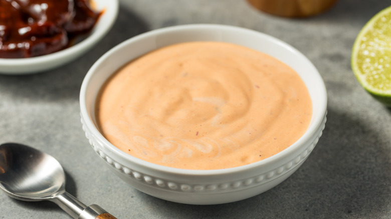 Homemade spicy mayo in bowl on a table next to other condiments.