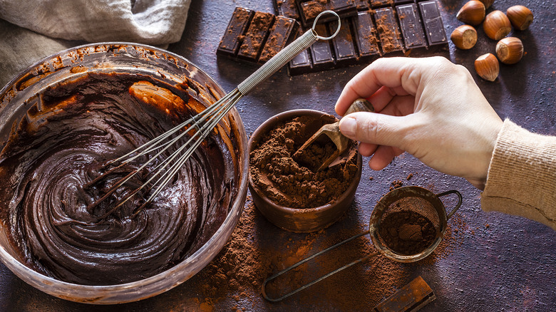 A bowl of chocolate cake batter next to cocoa powder and pieces of dark chocolate