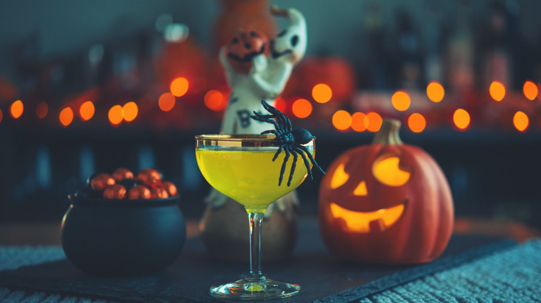 Halloween cocktail with jack o' lantern, bowl of candy, ghost decor, and fake spider