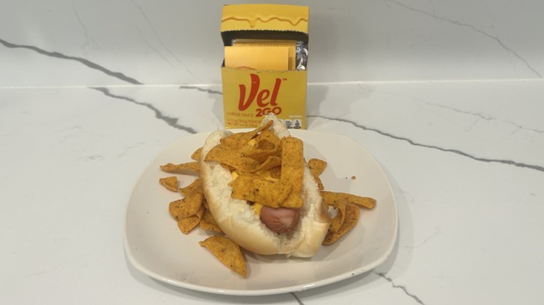 A hot dog is dressed with Velveeta cheese and Fritos Chili Cheese chips