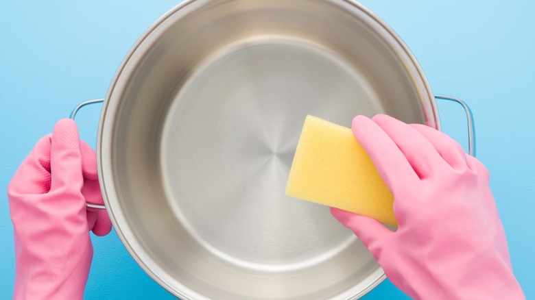 Gloved hands use sponge to clean stainless steel pot.