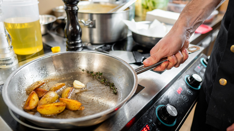 A chef holding a stainless steel pan with sliced potatoes over the stove