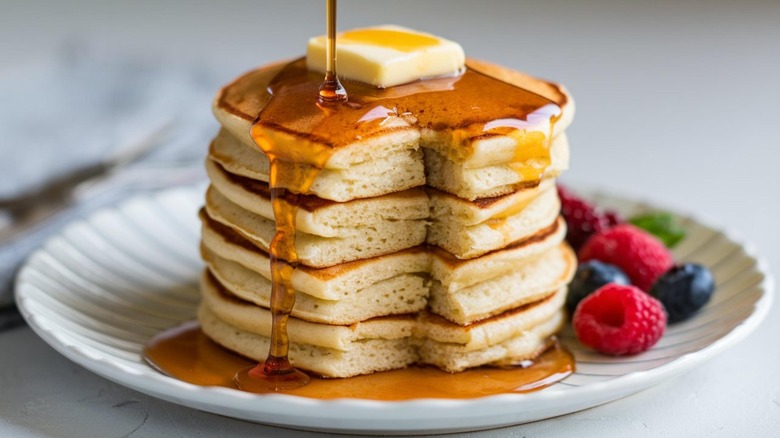 A stack of buttermilk pancakes with butter and syrup being poured on top