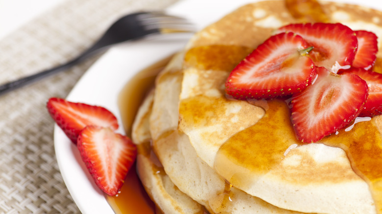 A stack of pancakes with syrup and sliced strawberries