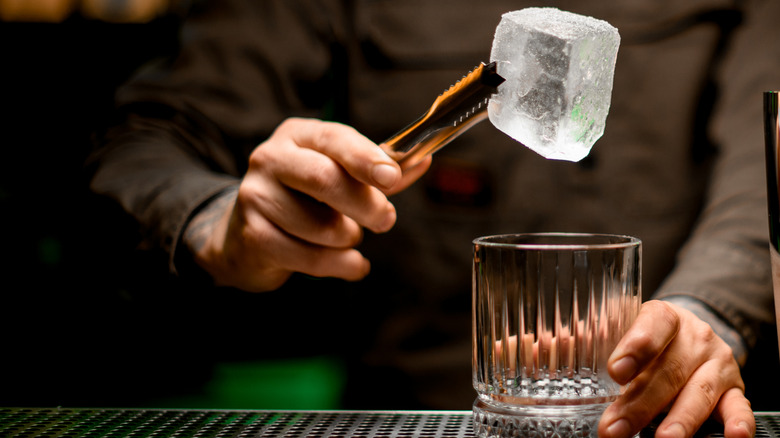 Bartender holding alarge icecube with tongs over a glass