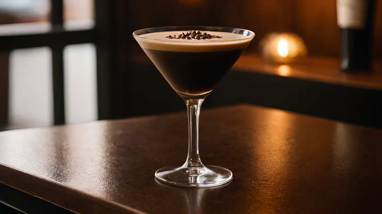 An espresso martini sitting on a wooden table with a candle in the background