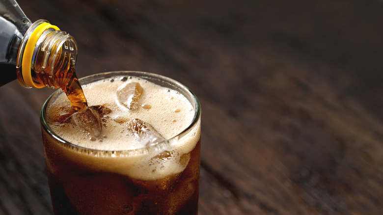 Soda being poured into a glass sitting on a wood table