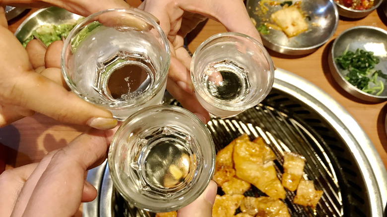 People holding glasses that contain soju.