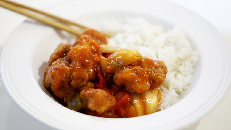 Sweet and sour chicken in a bowl with white rice and chopsticks