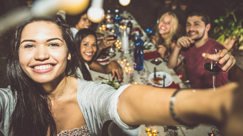 Friends enjoy barbecued meat and wine at outdoor dinner party