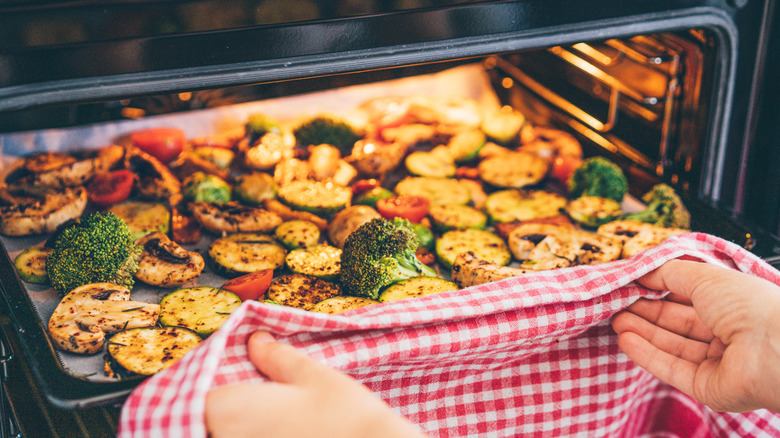 Person pulling tray of roasted veggies from oven