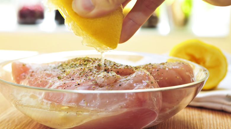 Chicken breasts in a glass bowl being covered with fresh lemon juice.