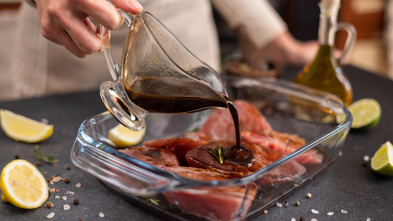 Person pouring a jug of marinade over tuna steaks in a glass dish