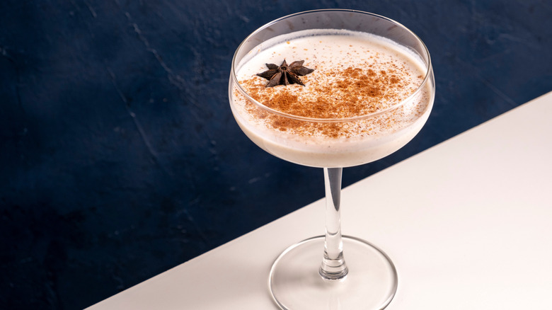 Eggnog sprinkled with fresh spices sits on a white counter in a cocktail glass.