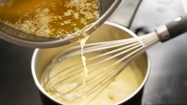 Butter being poured into hollandaise sauce in a pan with a hand whisk