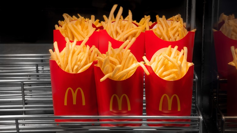 Six containers of McDonald's french fries sitting under a warmer