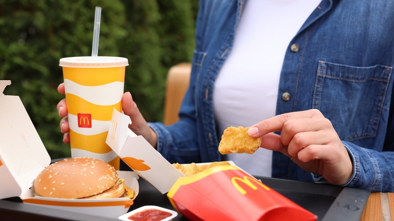 Person holding a fountain drink ad chicken nuggets over a tray