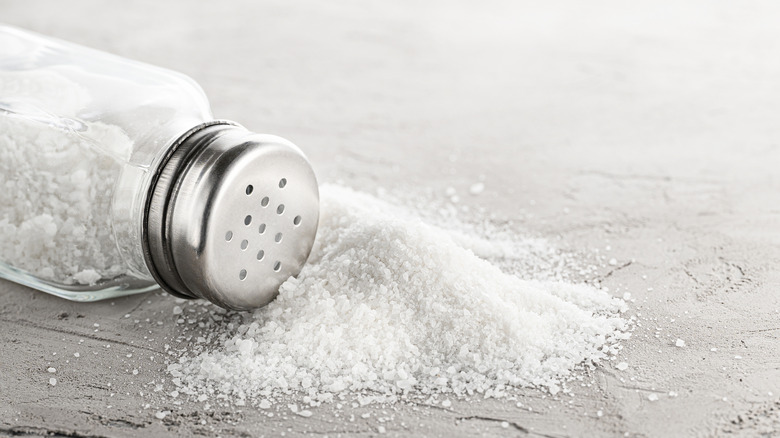 A close up of a bottle of salt on its side with salt spilling onto a counter