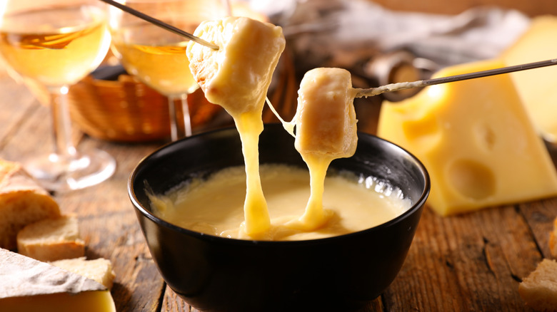 Person dipping a cube of cheese into a pot of fondue