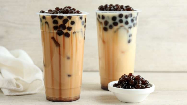 Two tall glasses of boba milk tea next to a bowl of tapioca balls