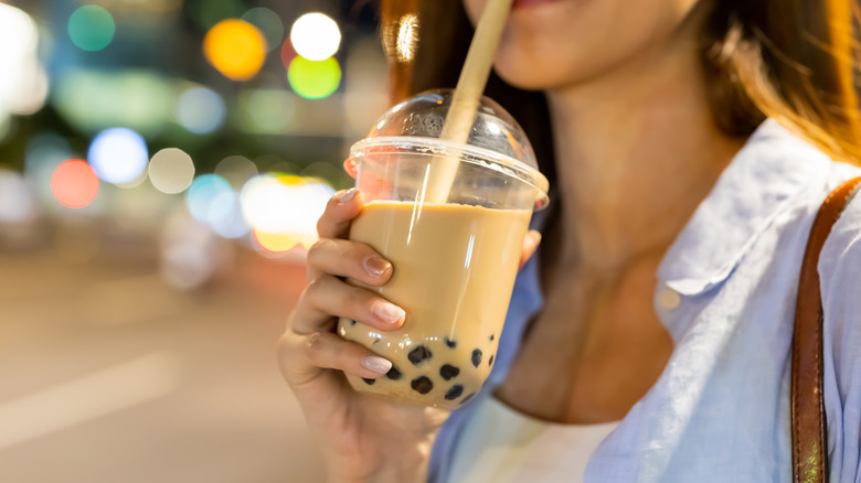 A woman drinking boba milk tea outside in a city