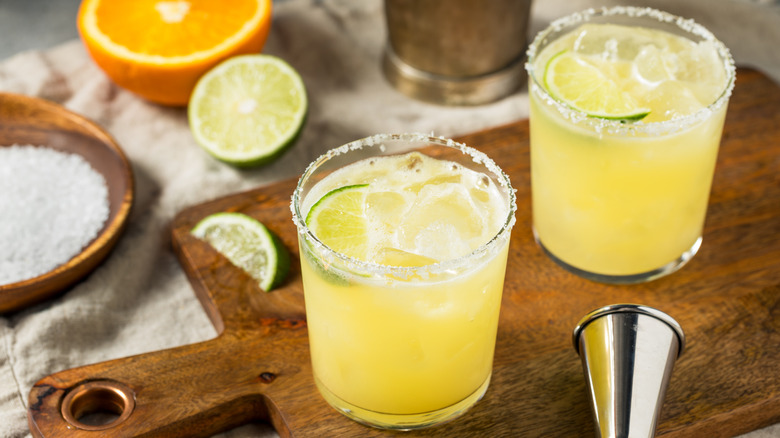 Two glasses full of margaritas with lime and orange slices nearby