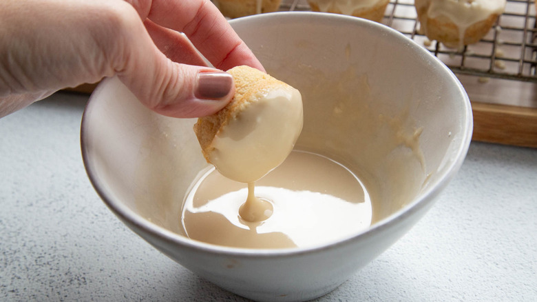 Hand dipping mini fritter into bowl of glaze