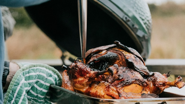 Person grilling chicken with lid in background