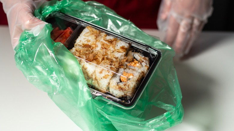 Pieces of suhi being placed in a to-go tray and bag