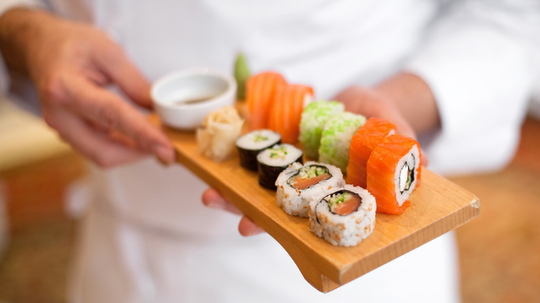 Sushi chef offering a wooden board of sushi