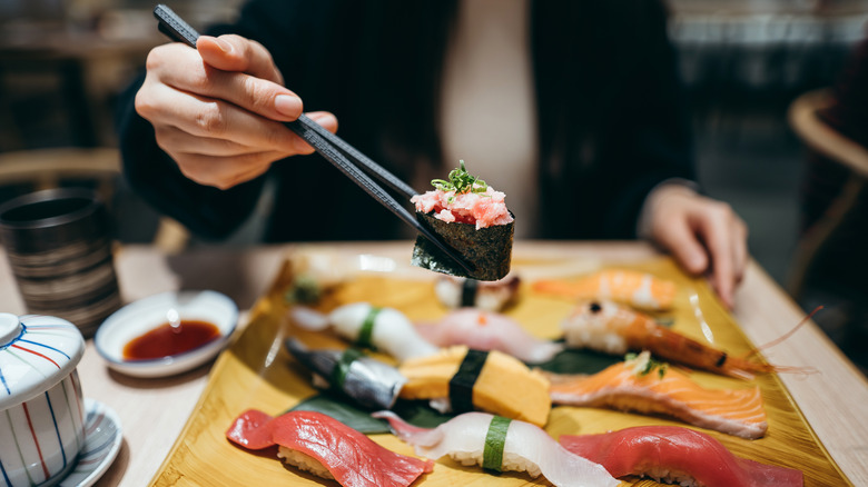 Woman holding out chopsticks with piece of sushi