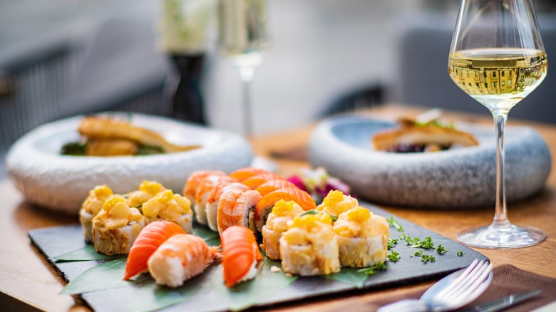 A tray of sushi on a table next to a glass of white wine