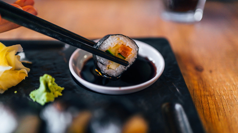 Close up of chopsticks dipping piece of sushi in soy sauce