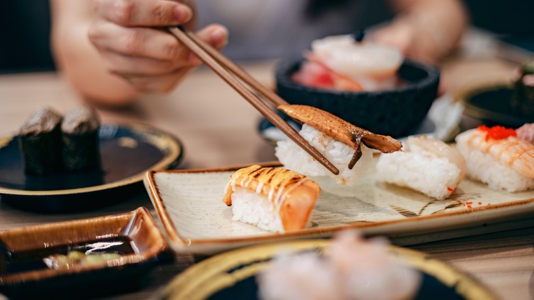 Woman picking up nigiri from tray with chopsticks