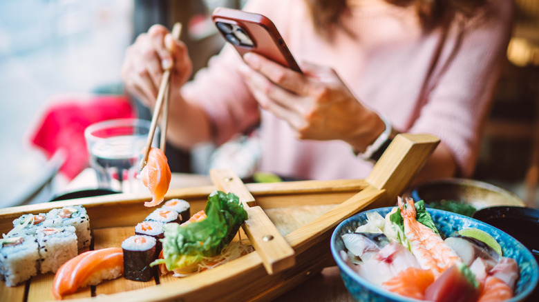 Woman using her phone to take a photo of a sushi tray