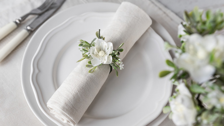 A white cloth napkin folded neatly on a dining plate with a flower napkin ring