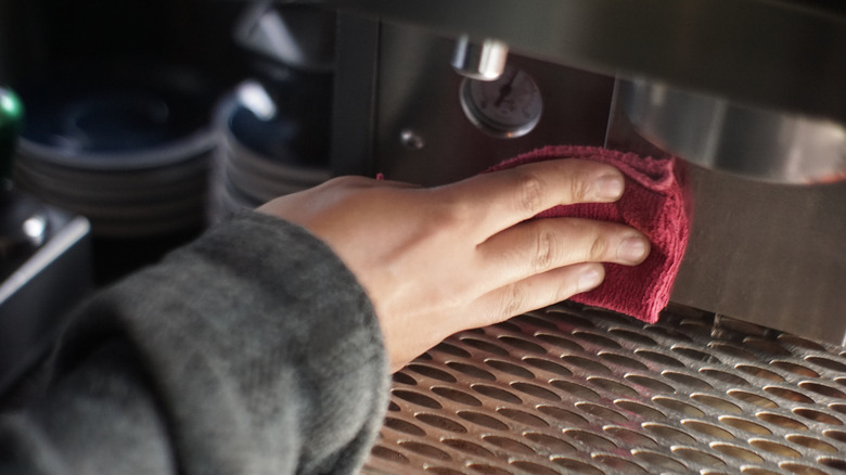 Person cleaning a coffee machine with a red rag