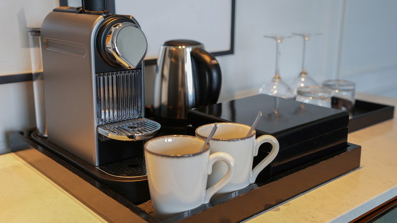 Nespresso machine sitting in a serving tray next to coffee mugs with spoons