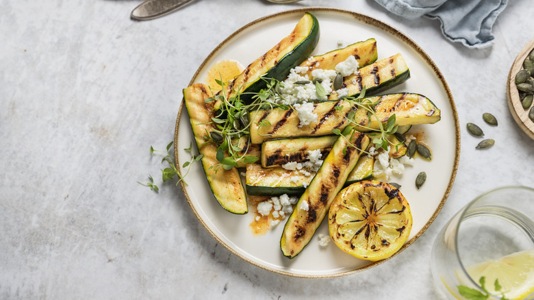 Grilled zucchini slices on white plate with slice of lemon