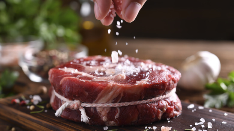 Fingers sprinkling salt on tied piece of red meat