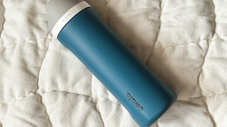 A blue Owala tumbler on a white comforter