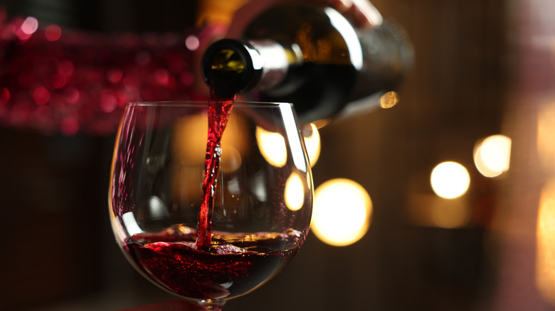 A person pouring red wine from a bottle into a glass