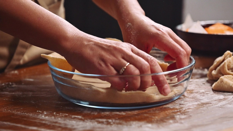 A cook lining a glass pie dish with pastry