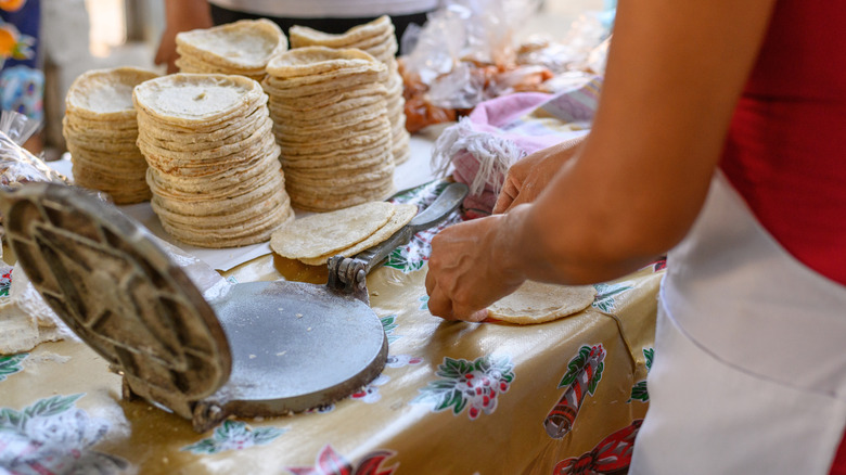 A cook making tortillas with a press machine at stall