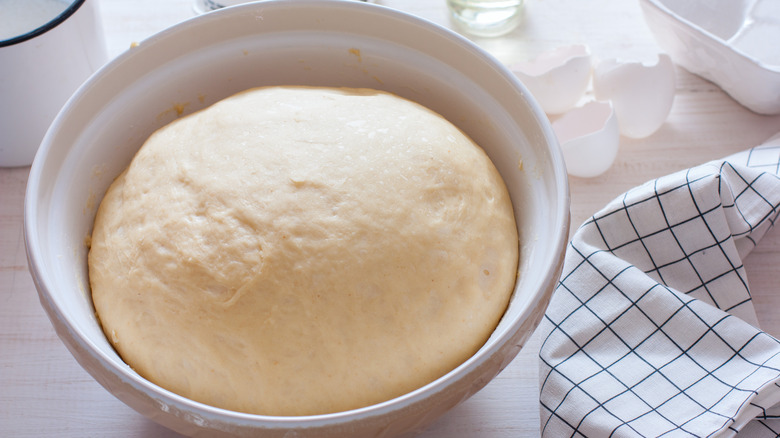 Bread dough proofing in a white bowl.